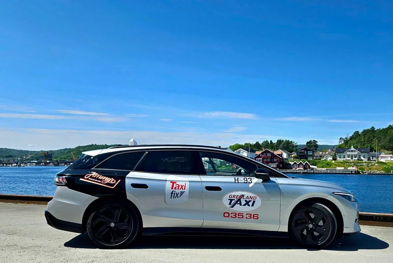 Sølvfarget elektrisk stasjonsvogn fra Grenland Taxi ved fjorden, med Grenland Taxi-logo og Taxifix-logo på siden