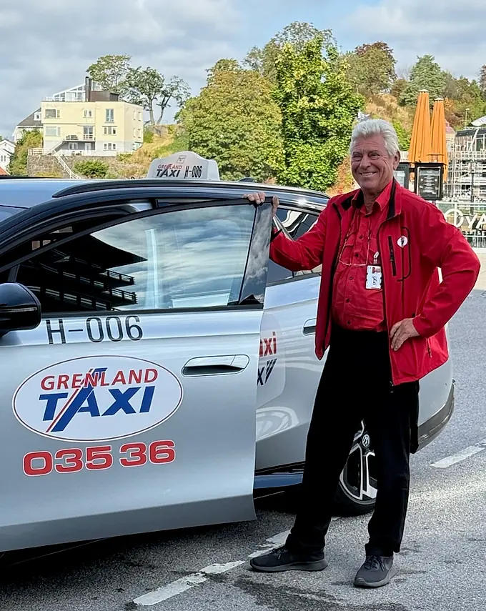 Sjåfør fra Grenland Taxi i rød jakke ved en sølvfarget elbil
